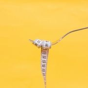 A fork holding a measuring tape over a yellow background to depict the relationship between food and weight.