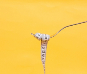 A fork holding a measuring tape over a yellow background to depict the relationship between food and weight.