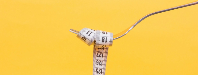 A fork holding a measuring tape over a yellow background to depict the relationship between food and weight.