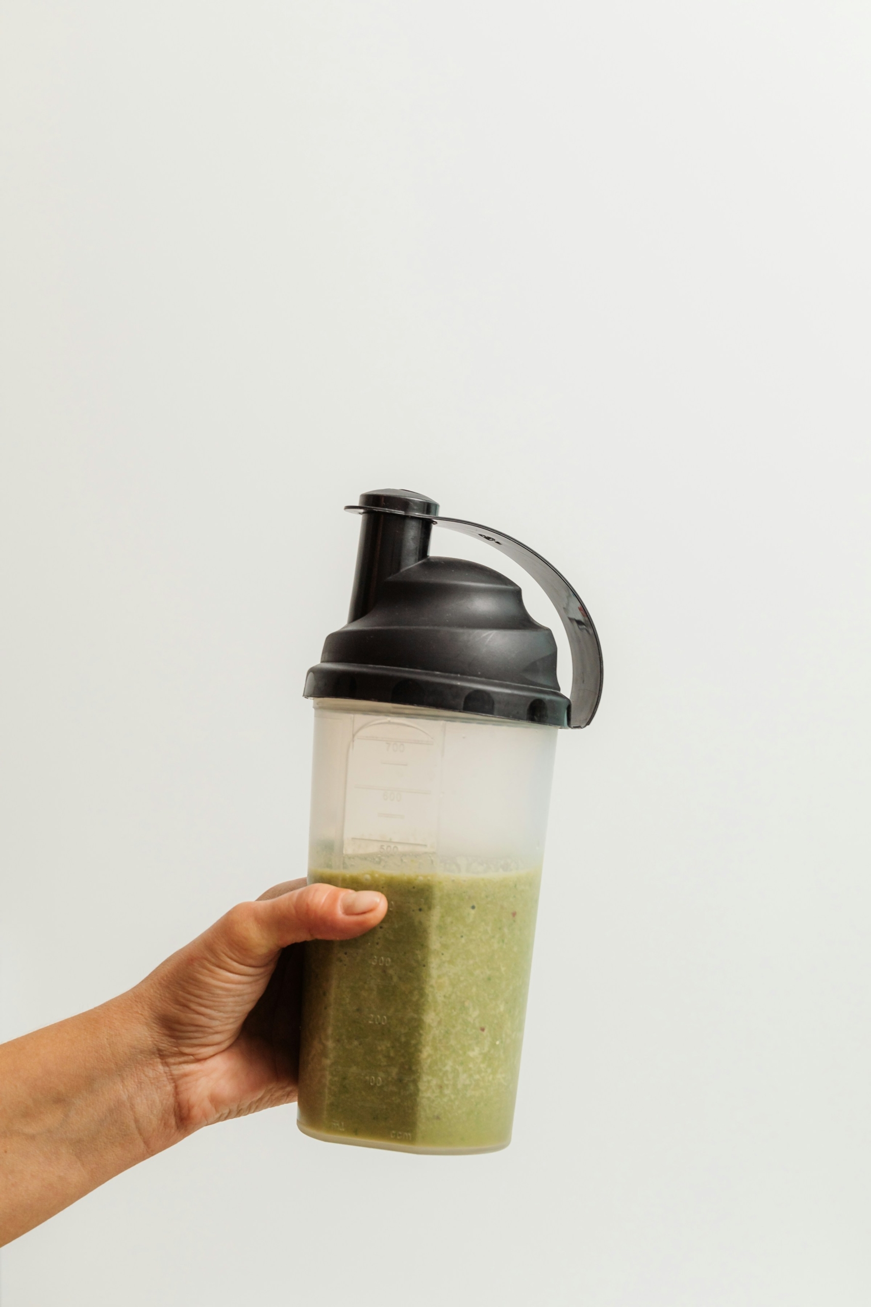 A hand holding a blender with a green smoothie in it