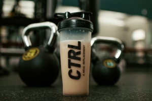 Protein shake on the floor, front layer with weights on the background out of focus