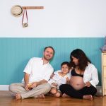 Photo of young cheerful positive smiling couple pregnant wife and husband with their son at home